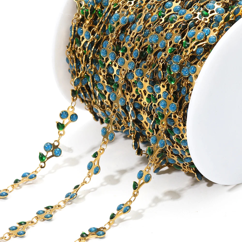 Close-up blue enamel cherry charm chain with gold links and green accents on a spool
