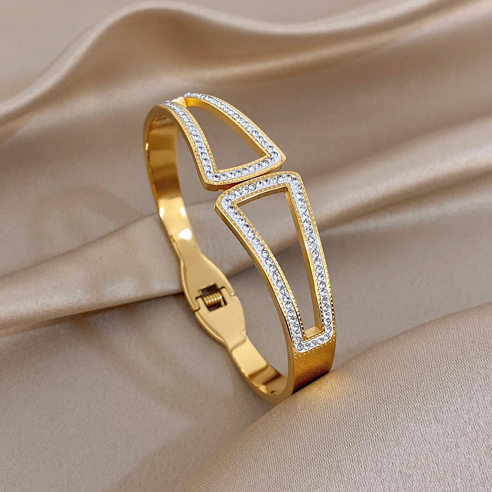 Gold-tone open geometric cuff bangle with clear rhinestone trim and hinge detail