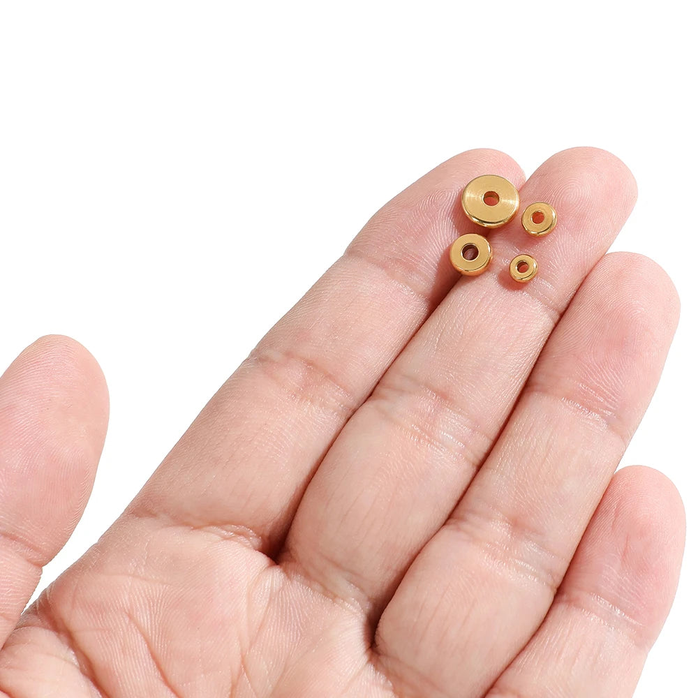 Gold round flat spacer beads held in an open palm, showing center holes