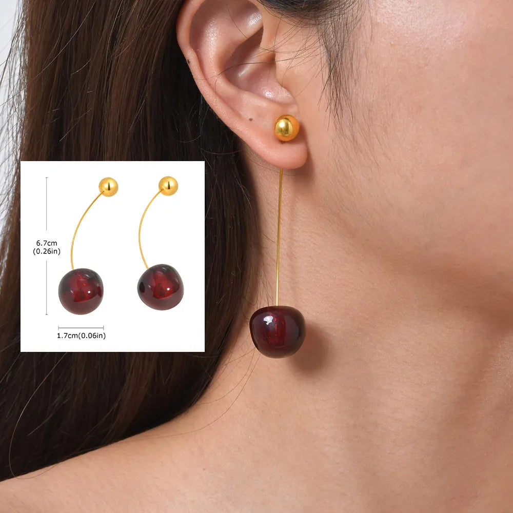 Gold-tone threader earrings with dark red ball drops, shown worn