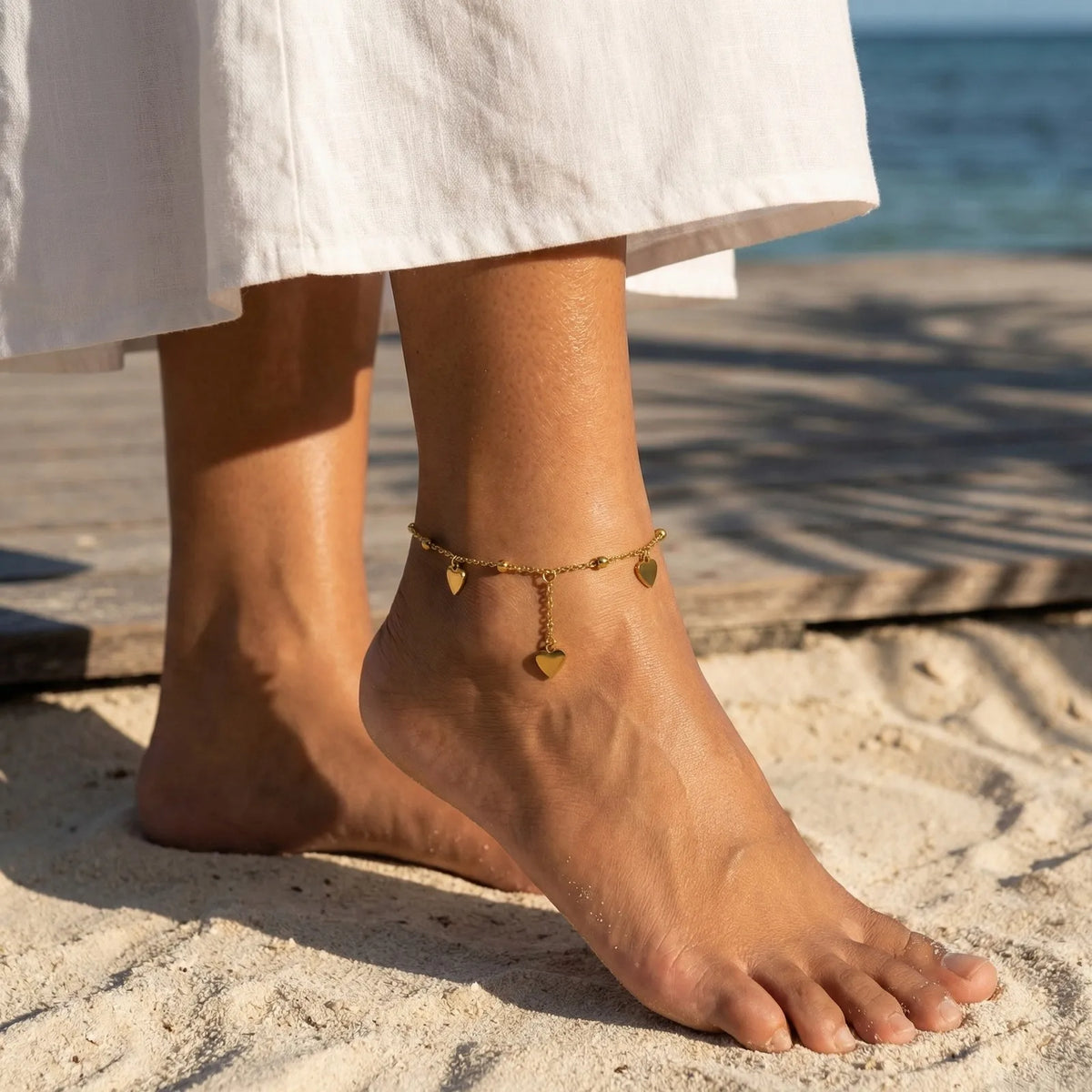 Gold-tone heart charm anklet with beaded chain and dangling heart pendant on ankle