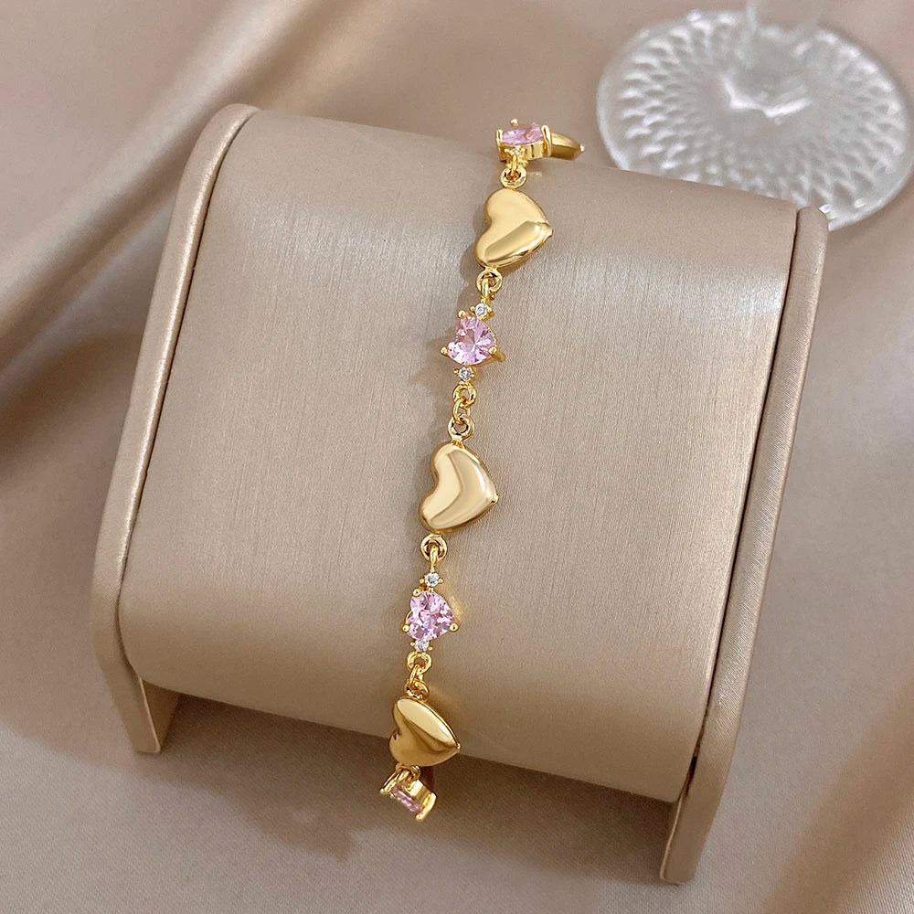 Gold-tone heart charm bracelet with pink crystal-like stones on a cuff display