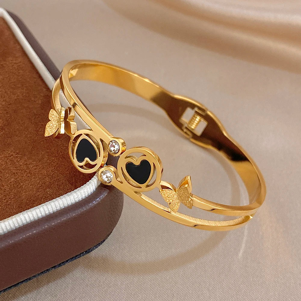 Gold-tone cuff bangle showing black enamel heart circles, crystal stones, and butterfly charms