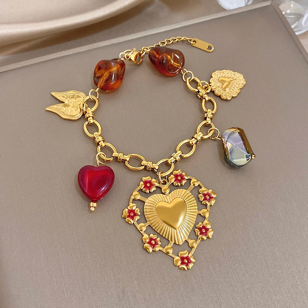 Gold-tone charm bracelet with red heart charm, amber beads, heart pendant, and wing charms