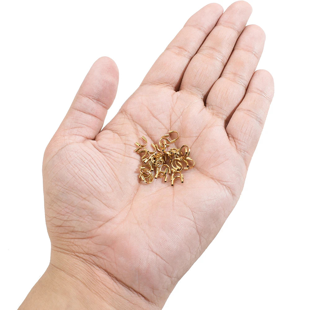 Gold U-shaped wire protectors held in palm, small connector clasps for DIY jewelry