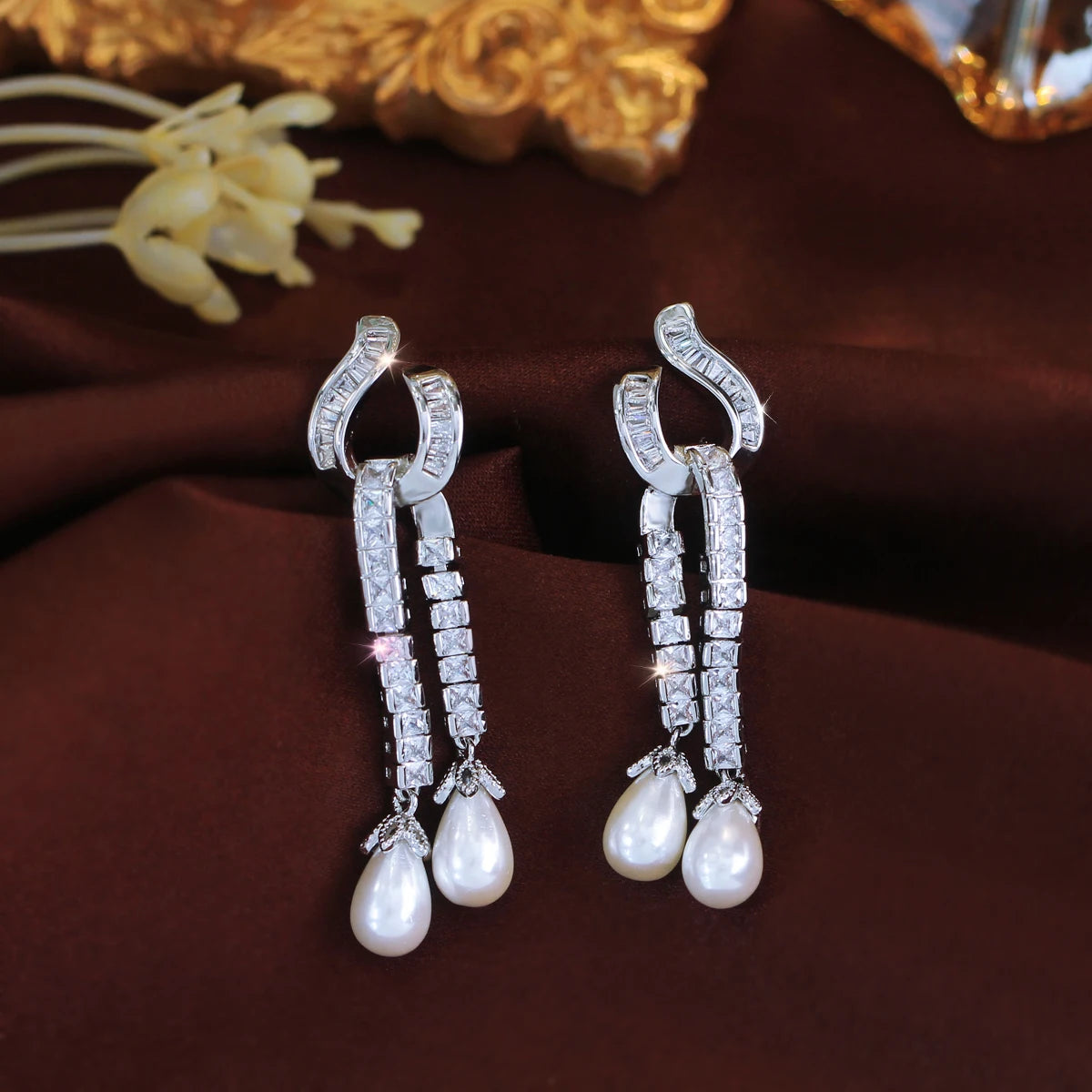 Pair of silver-tone zirconia dangle earrings with curved tops and two pearl drops each.