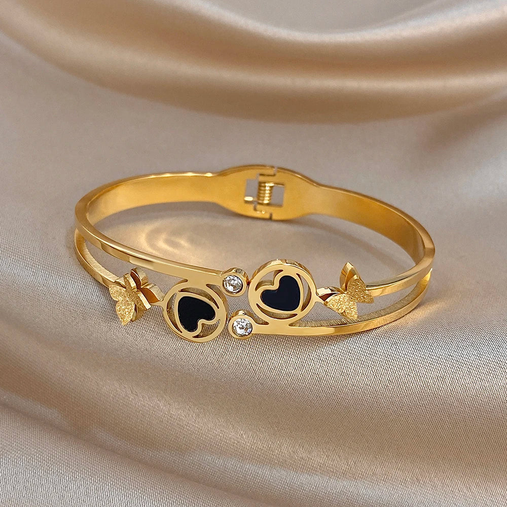 Gold-tone wide cuff bangle with black enamel heart motifs, butterfly charms, and crystals