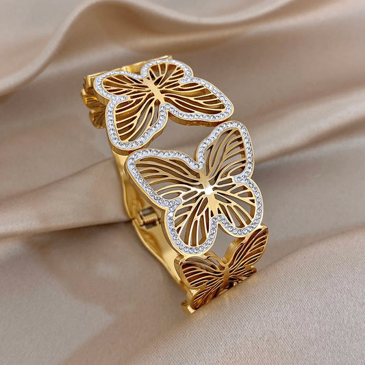 Gold-tone wide cuff bracelet with butterfly charms and clear rhinestone edging