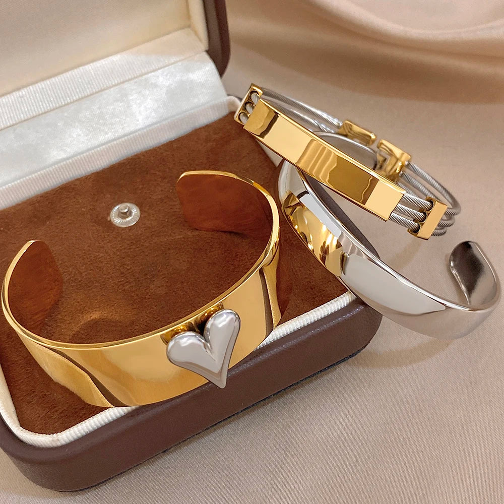 Gold and silver cuff bangles with heart charm and geometric clasp on shiny metal
