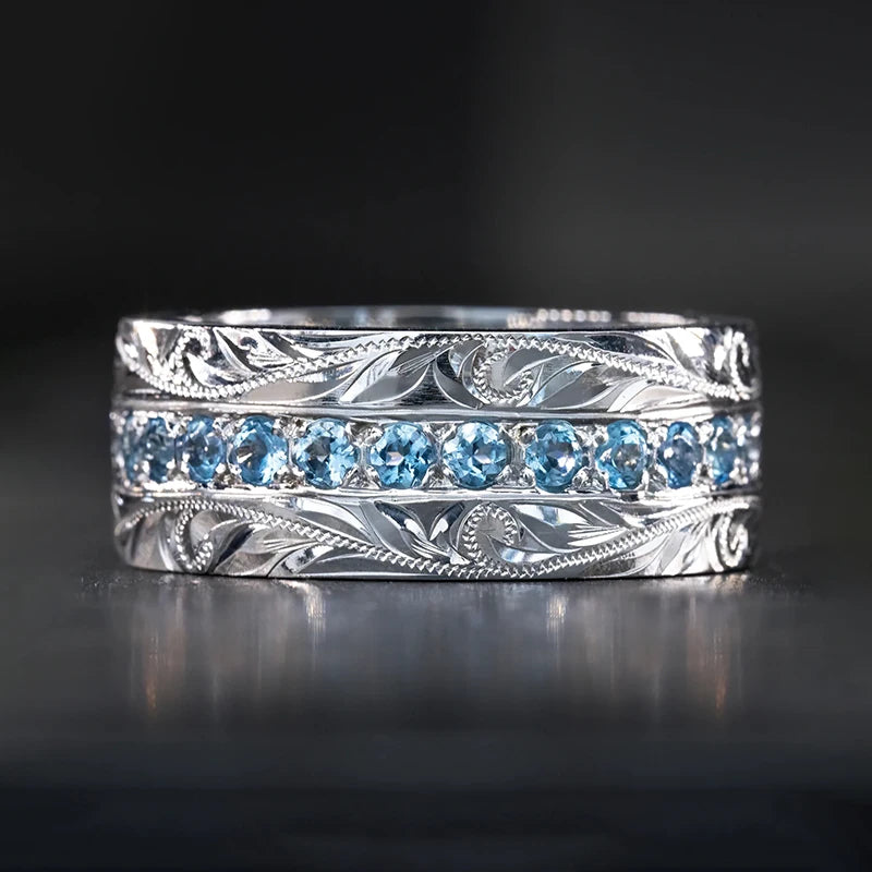 Silver engraved wedding band with blue channel-set stones and ornate filigree edges
