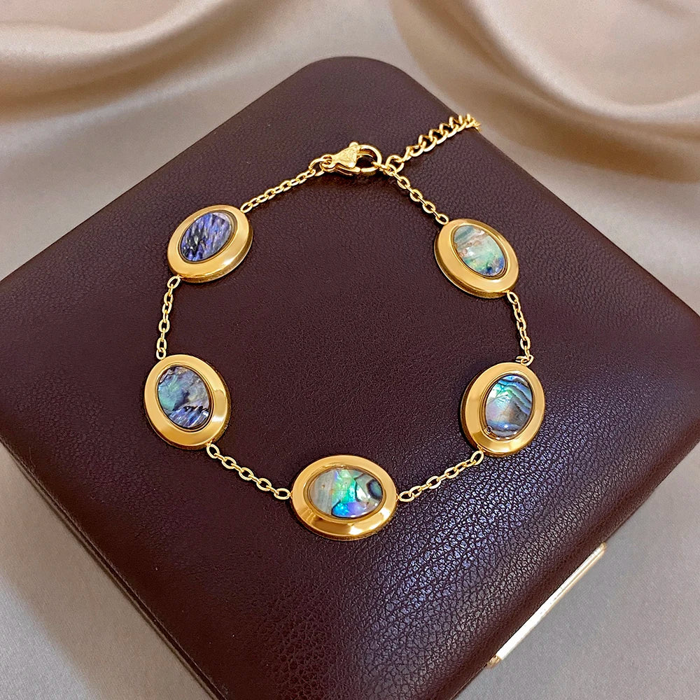 Gold plated oval link bracelet with blue and iridescent abalone shell bezel charms