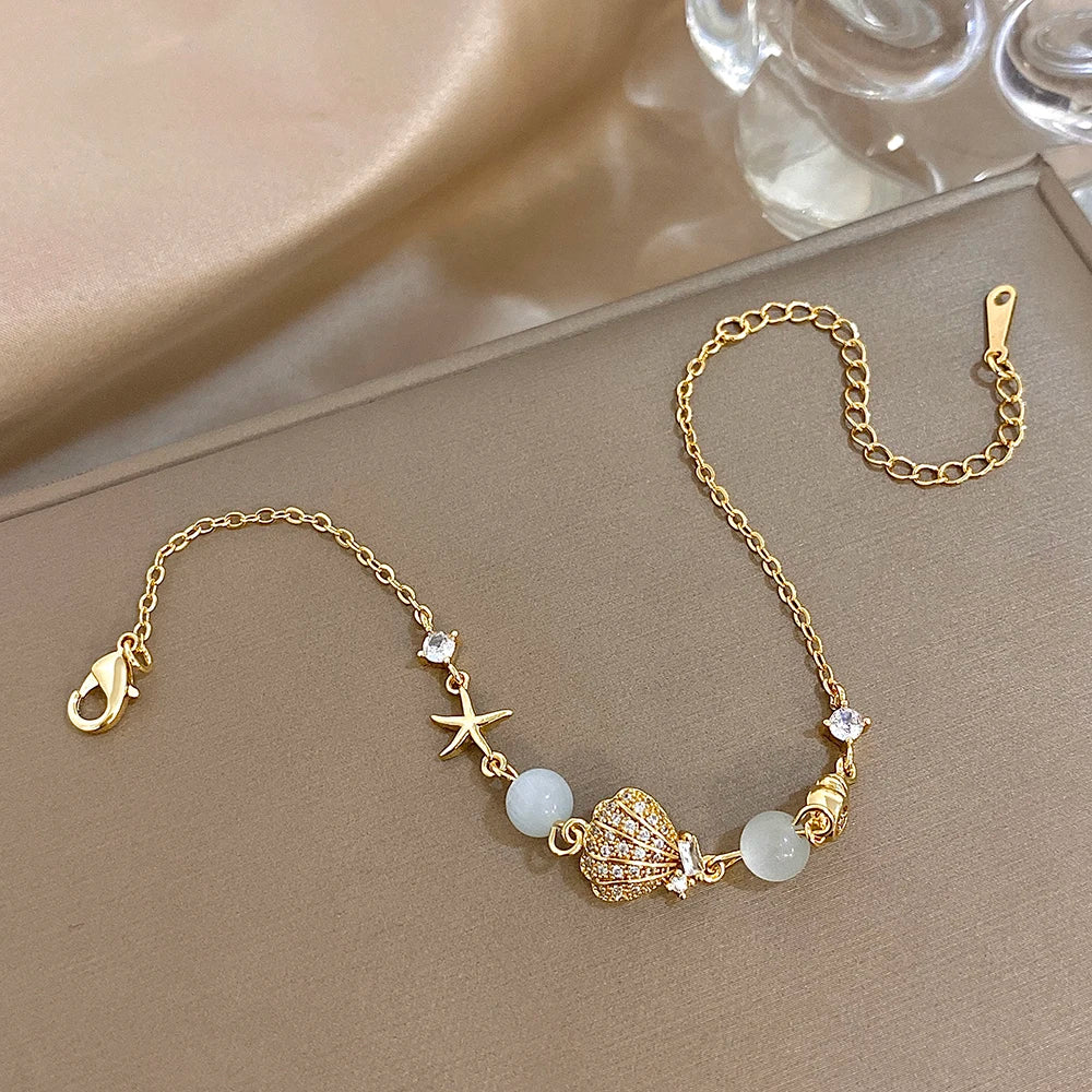 Gold-tone shell and starfish charm bracelet with moonstone-style beads and rhinestone charms