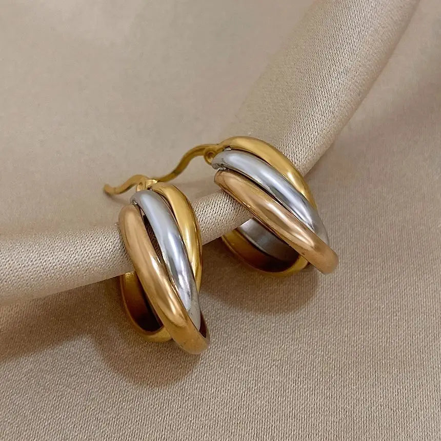 Close-up of gold, silver, and rose-gold bands on twisted hoop earrings