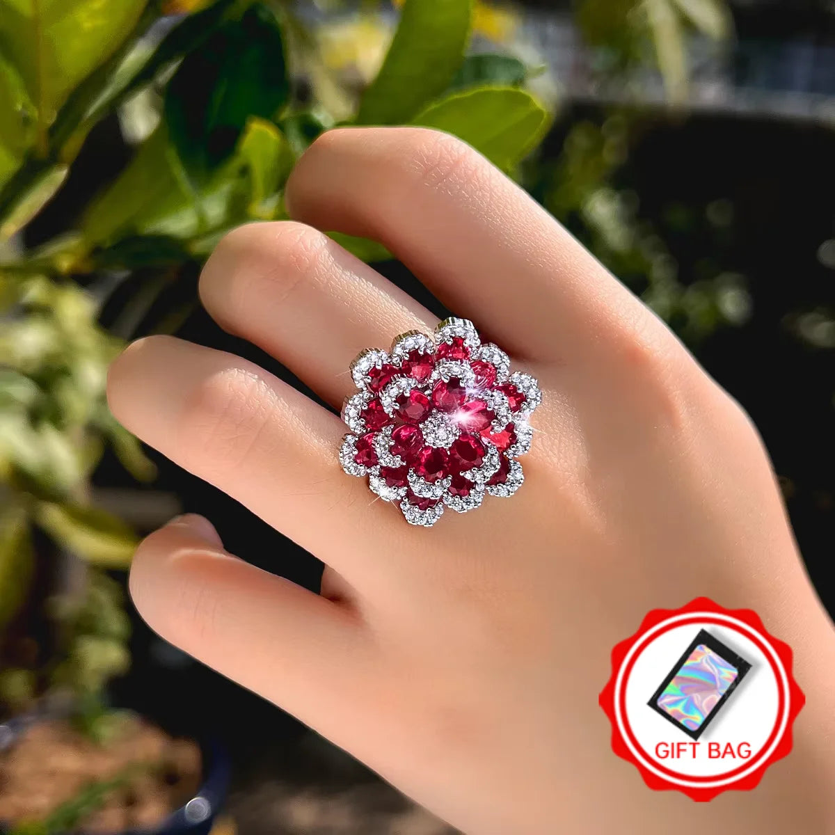 Red and clear stone flower ring worn on a hand; gift bag included