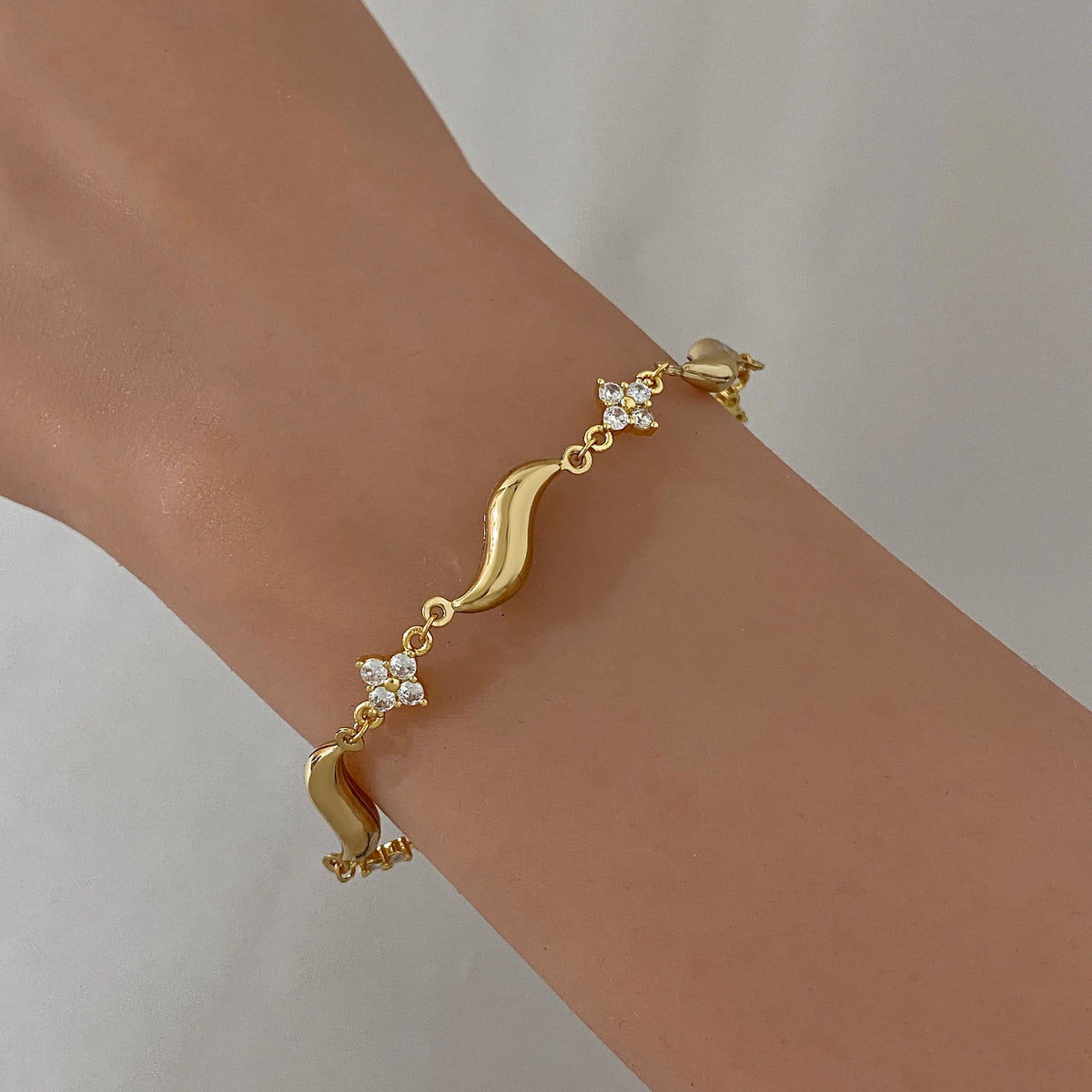 Gold-plated wave bracelet on wrist with small crystal flower details and clasp