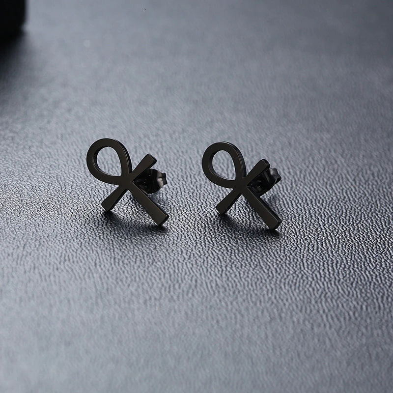 Black ankh cross stud earrings, close-up on textured surface