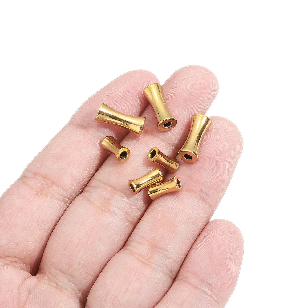 Gold tube spacer beads in hand, small metal cylinders with through-holes and open ends