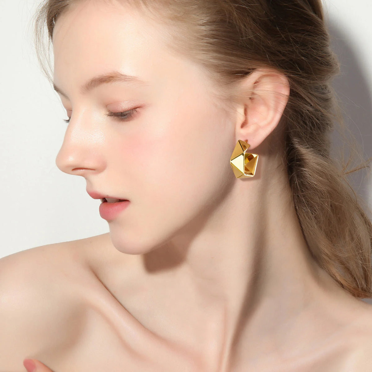 Gold-plated geometric hoop earrings on model ear, faceted angular design