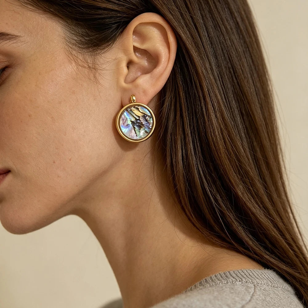Gold-tone round abalone shell hoop earrings worn on ear, iridescent center