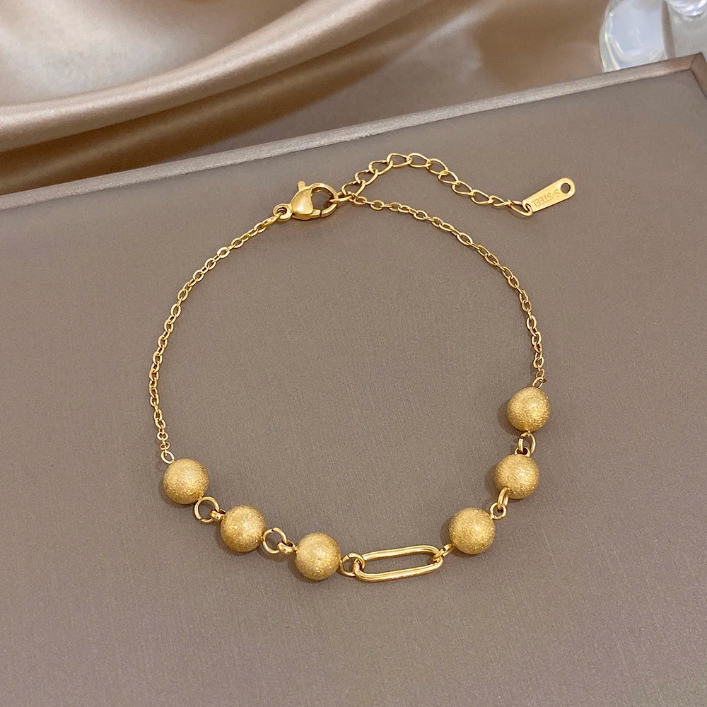 Gold-tone slim chain bracelet with round bead charms and clasp tag