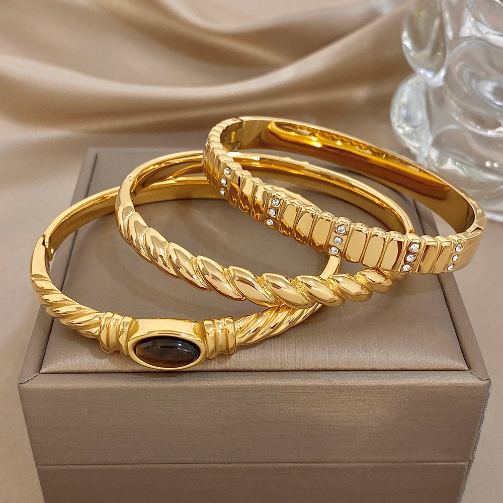 Set of gold-tone twisted cuff bangles with dark oval stone and crystal rows