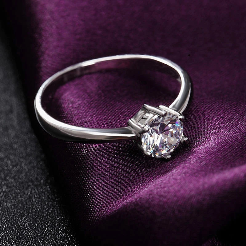 Silver-tone six-prong round cubic zirconia ring on dark purple fabric, close-up