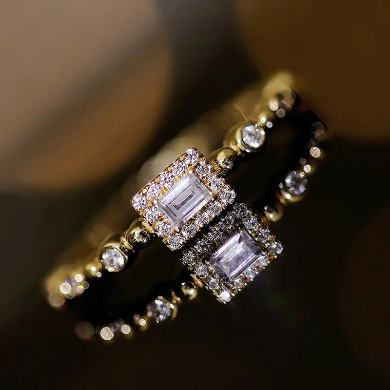 Pair of gold-tone square halo rings with baguette centers and round accents