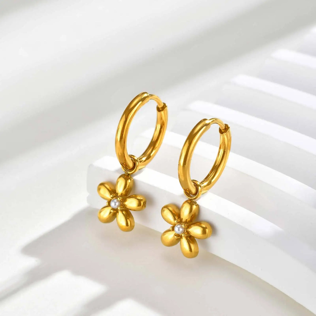 Pair of gold hoop earrings with dangling five-petal flowers and clear stone centers.