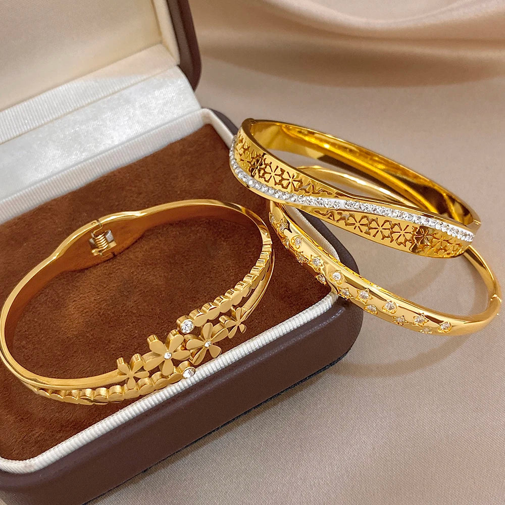 Gold cuff bangles with clear stone rows, geometric engraving, and daisy detail