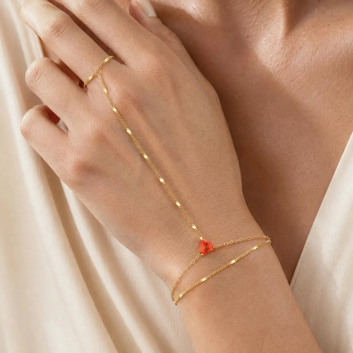 Gold-tone hand chain bracelet with red teardrop stone and CZ accents