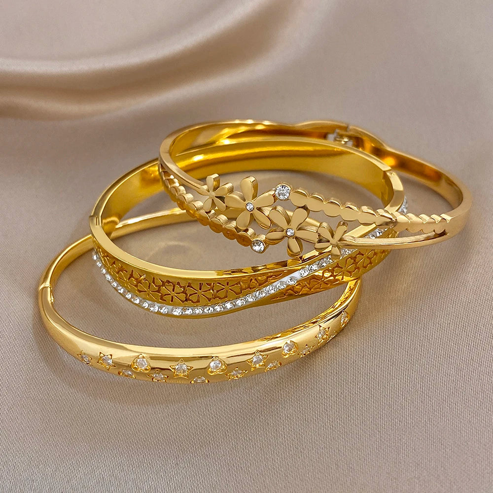 Stack of gold cuff bangles with daisy charms, etched bands, and clear crystal insets