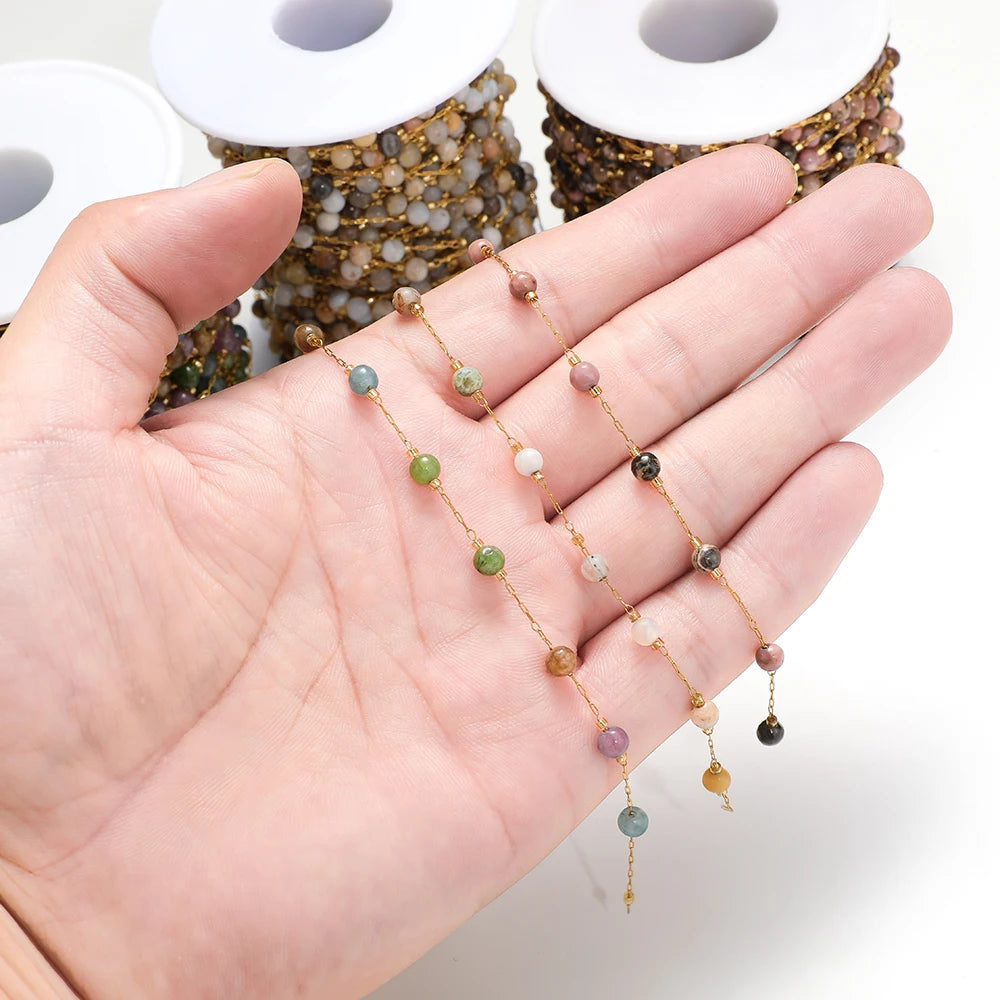 Hand holding gold-link gemstone bead chains with pink, teal, green, and white beads