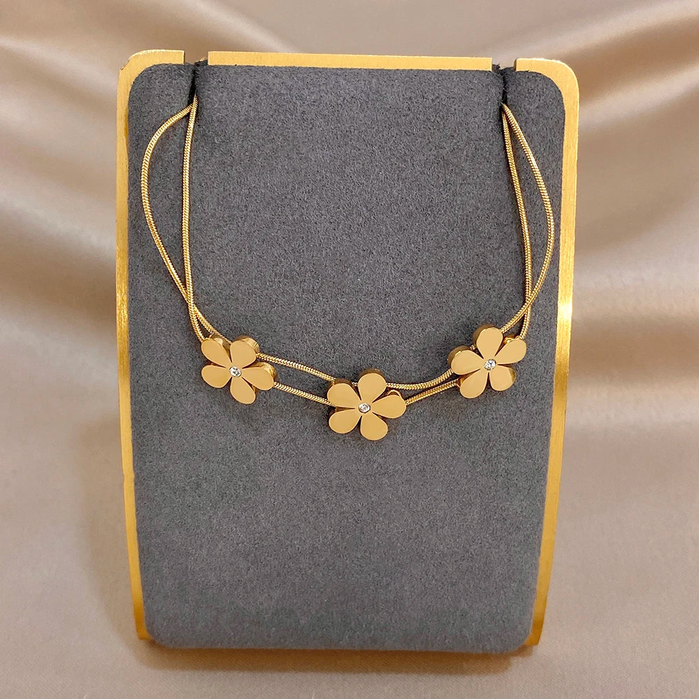 Gold double-layer snake chain bracelet with five flower charms and crystal centers on a display card