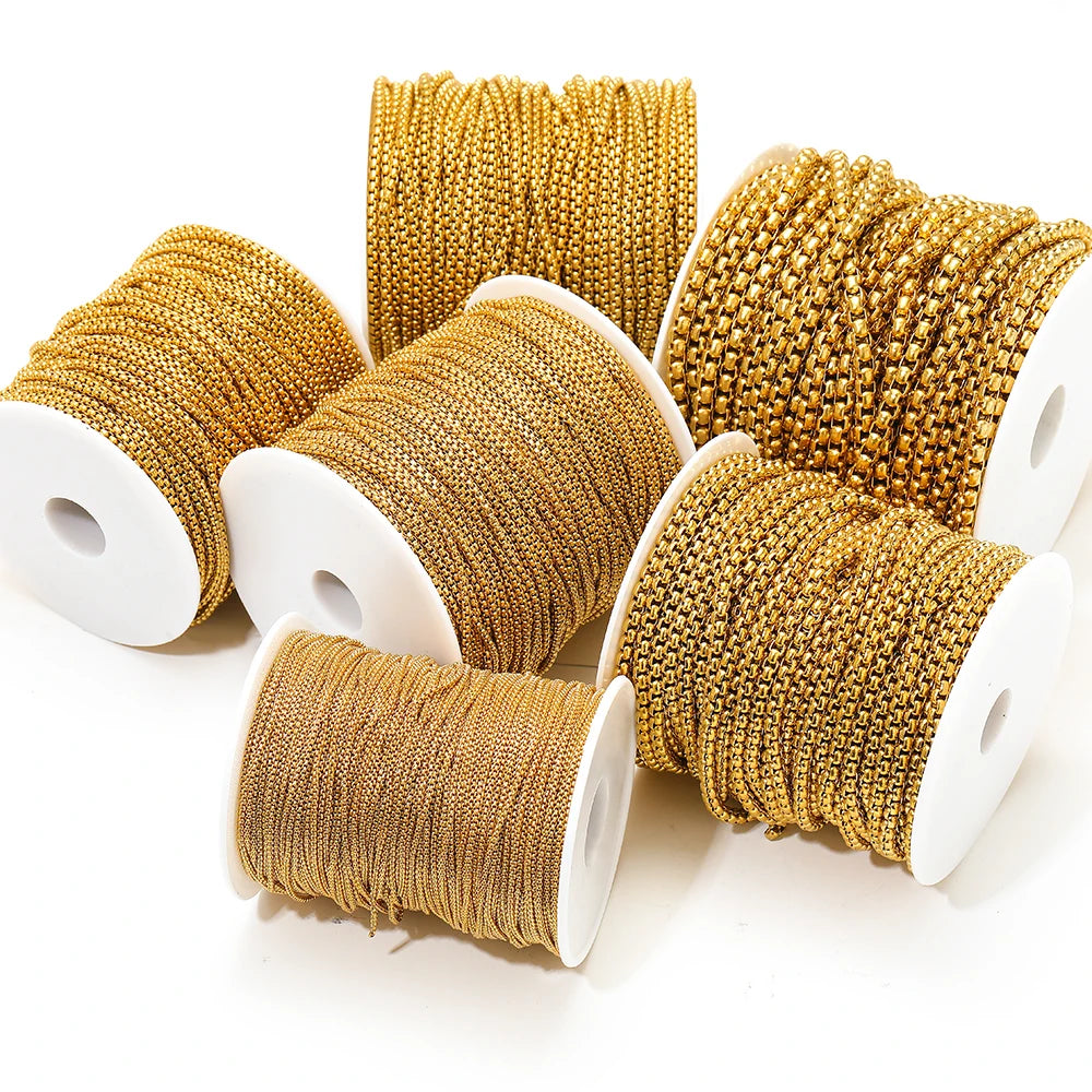 Gold rolo box chain on white spools, rectangular mesh-like link pattern