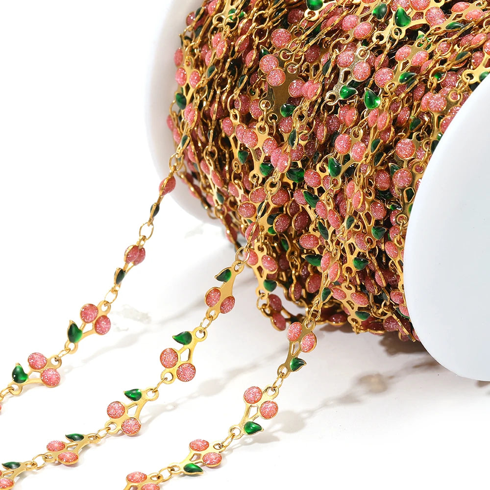 Close-up cherry charm chain with gold links and pink enamel flowers, green and red accents