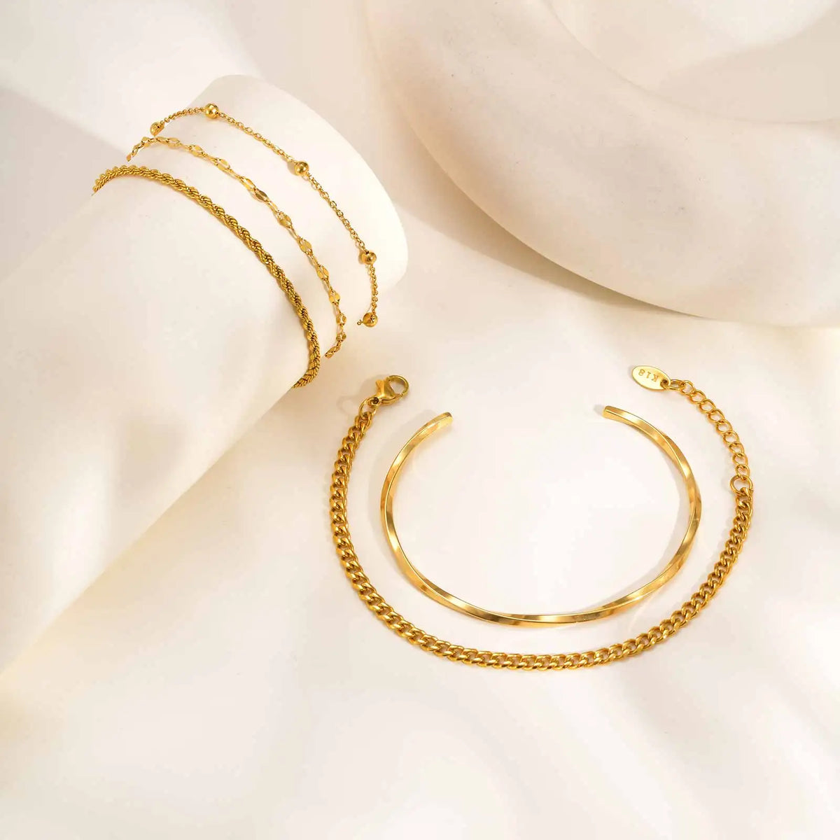 Gold tone chain bracelet stack with linked bands and smooth open cuff bangle