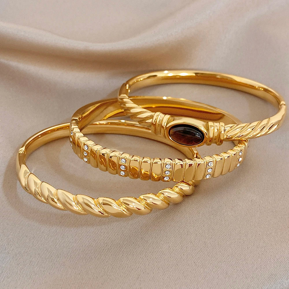 Gold-tone twisted cuff bangles with dark oval stone and crystal bordered band