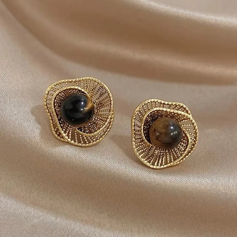 Gold-tone flower stud earrings with dark round bead and textured spiral center