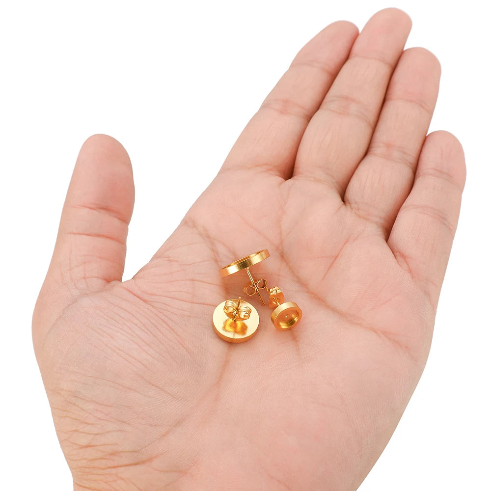Gold-tone round stud earring base settings with post and back, held in hand