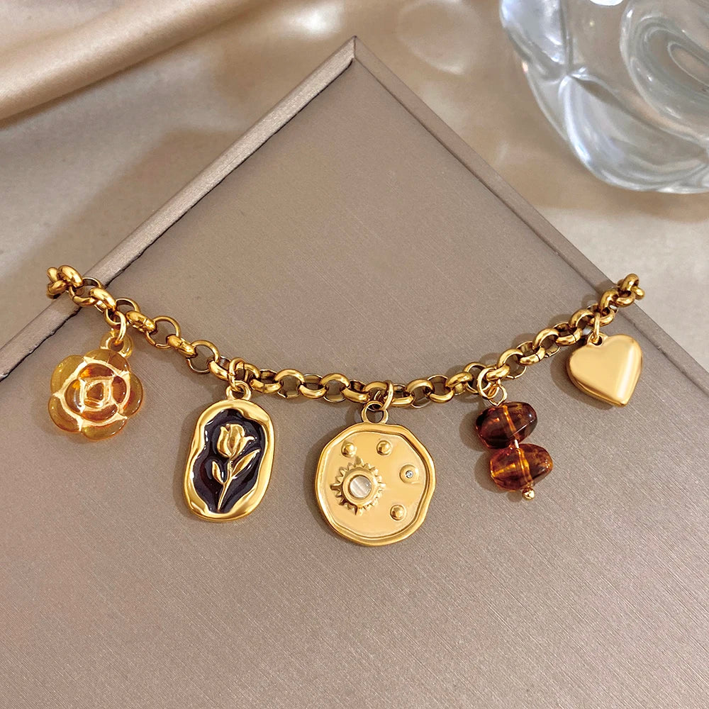 Gold plated charm bracelet with rose, leaf, round gear coin, heart, and amber beads