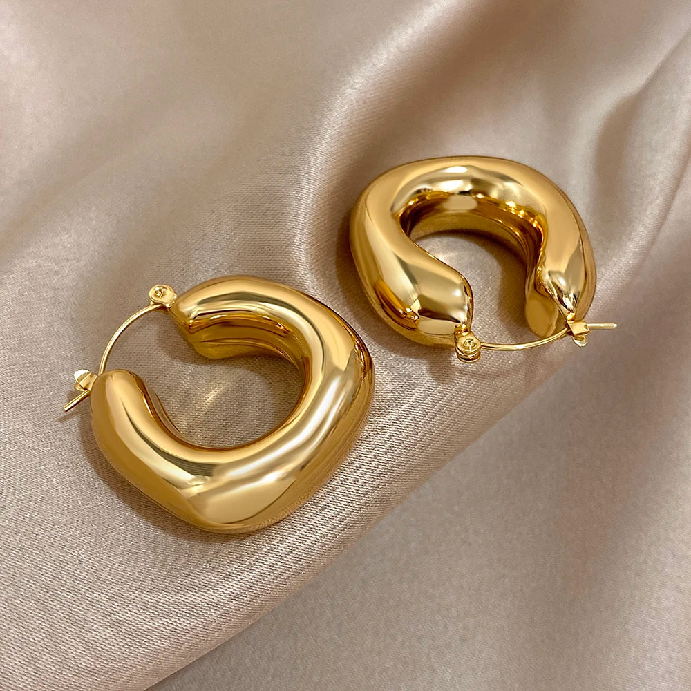 Chunky gold-tone hoop earrings with open ends and curved, sculptural fronts