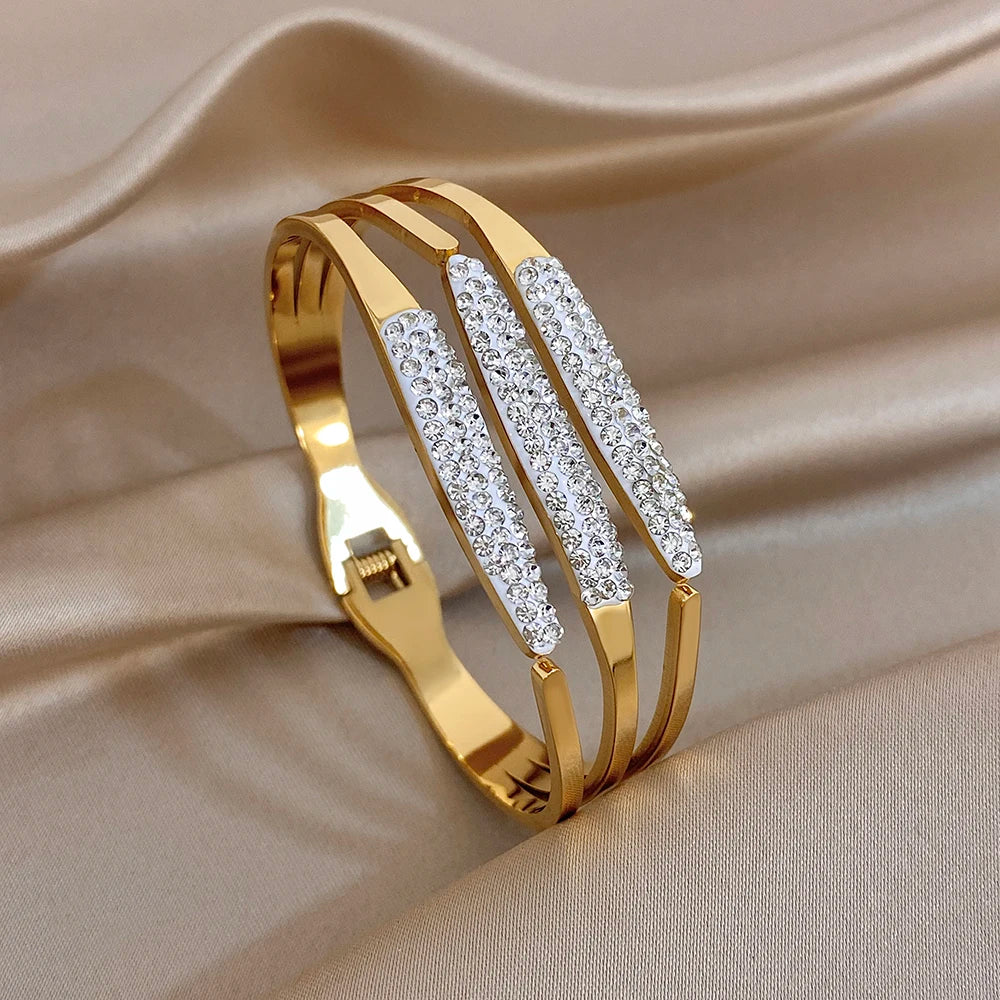 Gold-tone wide cuff bangle with three rhinestone inlaid bars on hinged opening