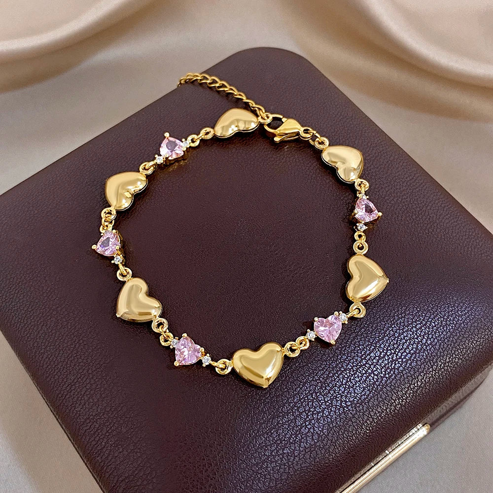 Gold-tone heart link bracelet featuring pink crystal-like stones and heart charms