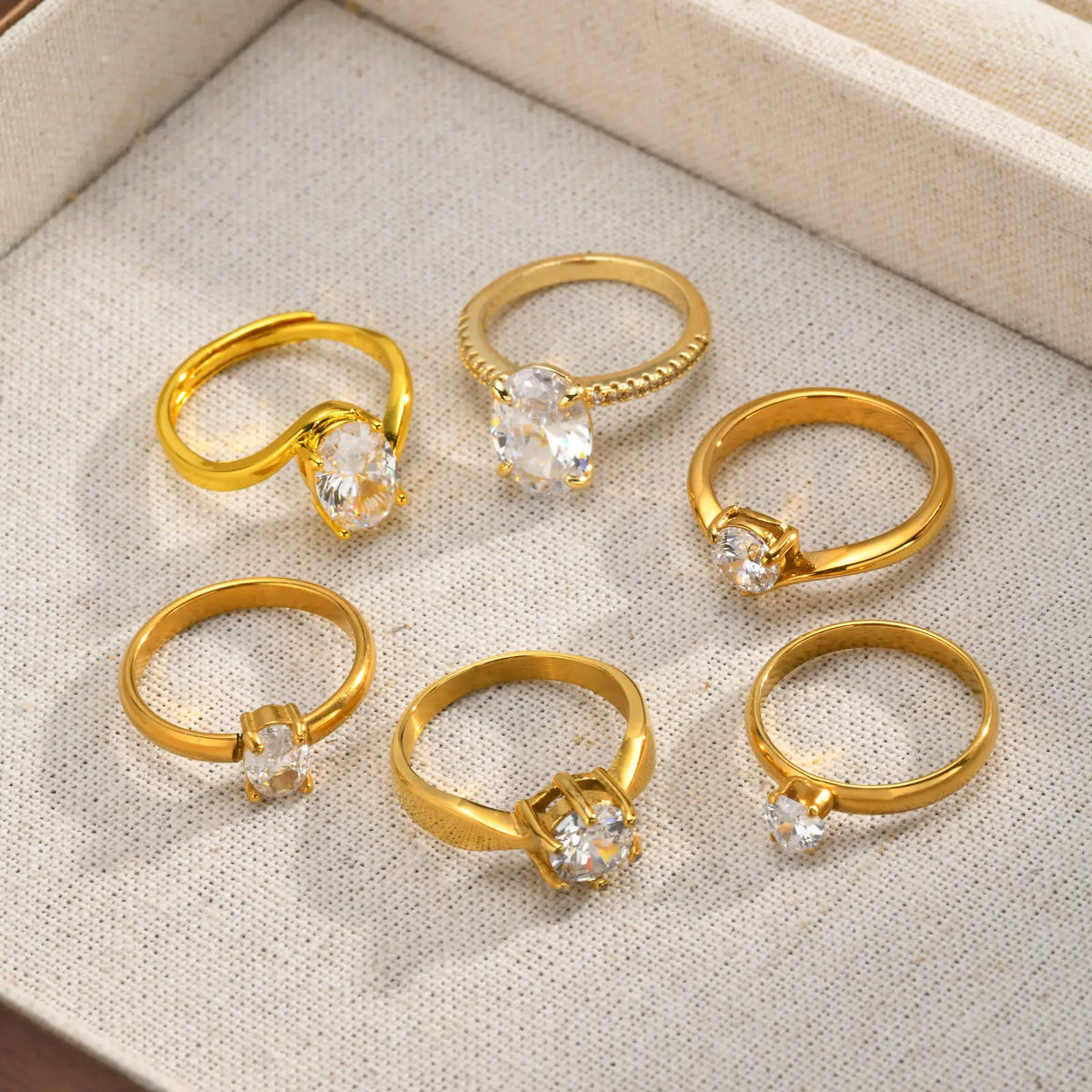 Five gold-tone open-band cubic zirconia rings displayed on beige fabric