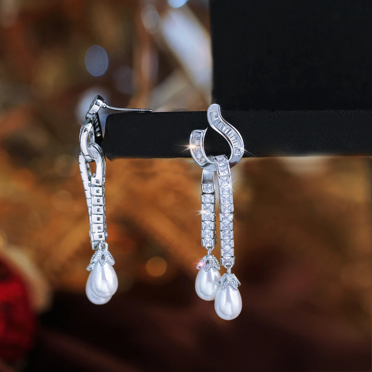 Side view of silver-tone zirconia dangle earrings with pearl drops and hinged backs.
