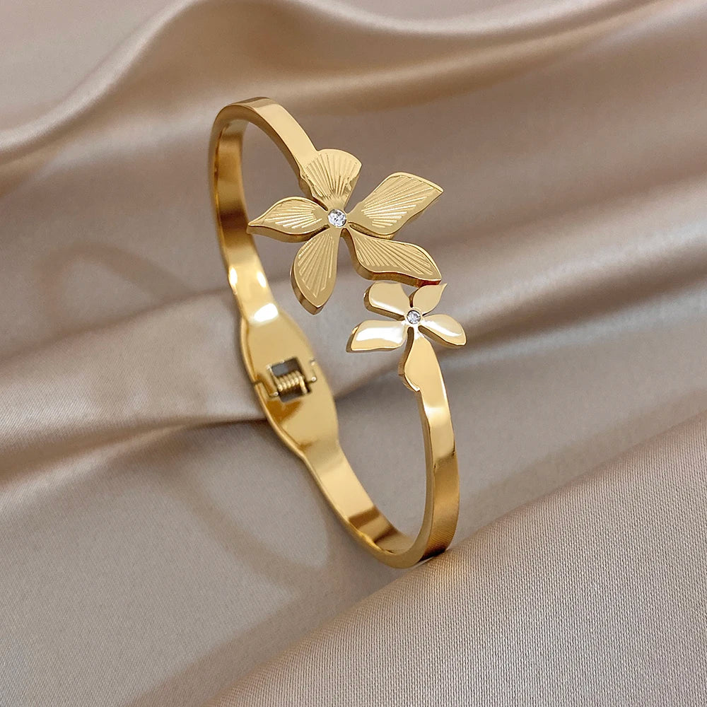 Gold-plated cuff bangle featuring a flower and leaf charm with small zircon stone centers