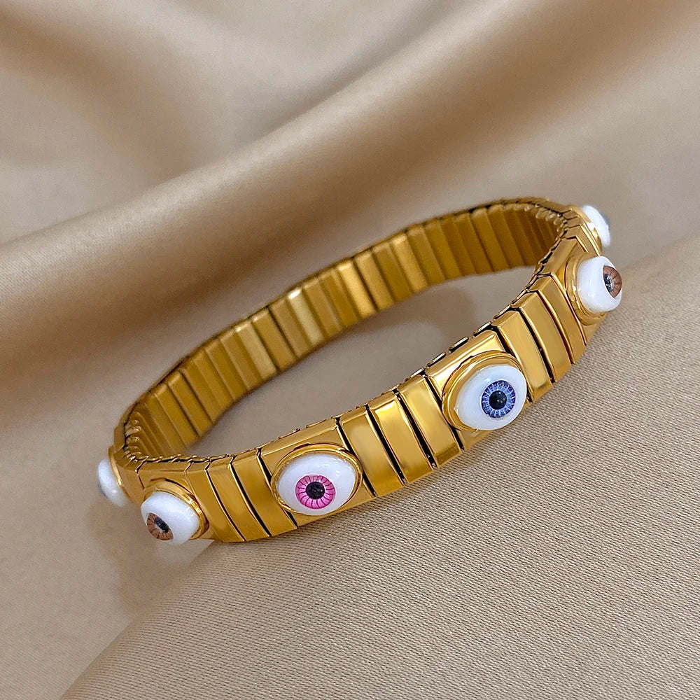 Gold-tone elastic bracelet with oval evil eye insets along a ridged metal link band