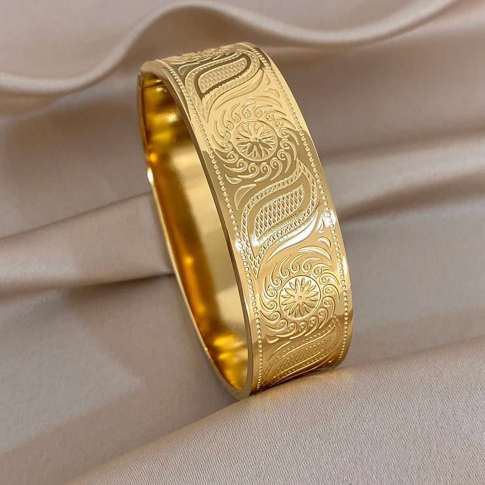 Gold-tone wide cuff bangle with engraved floral swirls on geometric textured surface