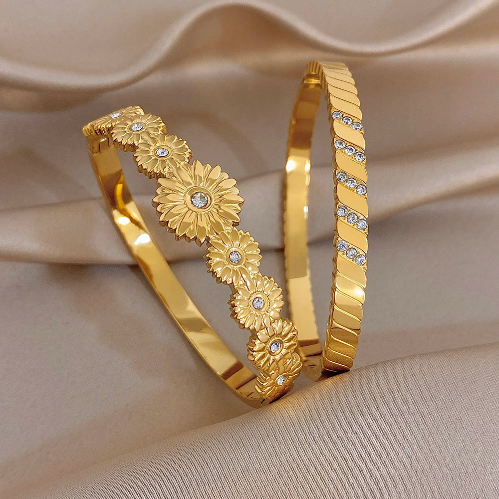 Two gold tone cuff bangles with floral medallions and clear rhinestone stripe