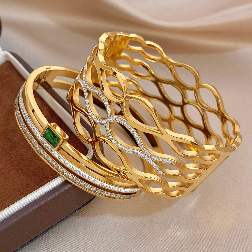 Gold-tone open cuff bracelet with diamond-like stones, green square detail, and stacked bangles